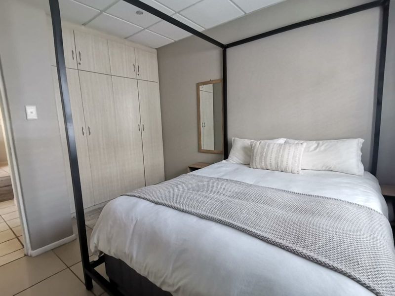 A well-maintained bedroom featuring neutral-toned built-in cupboards, tiled flooring, and a modern drop ceiling design.