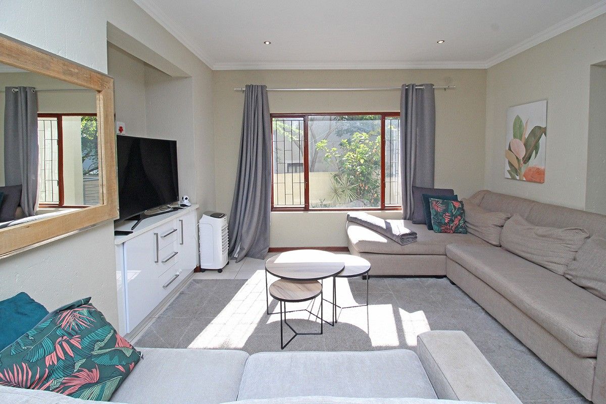 A well-maintained living room featuring built-in cabinetry, recessed downlighting, and a large window with security bars, providing a comfortable and functional space.