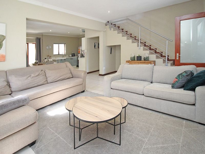 Spacious open-plan living area featuring a modern staircase with metal balustrade, neutral tiled flooring, and recessed lighting, flowing into the adjacent kitchen space.