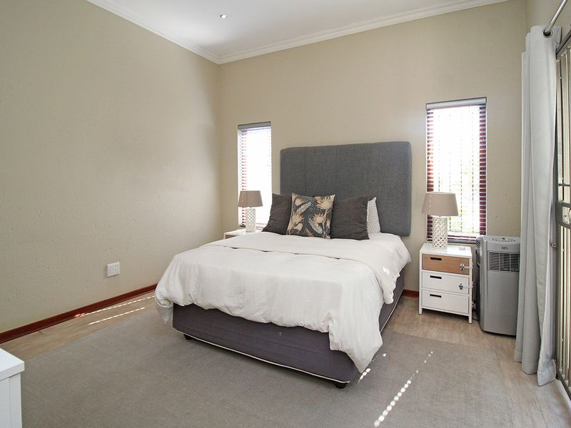 A well-maintained bedroom featuring neutral walls, light flooring, recessed downlighting, and dual windows fitted with venetian blinds and a security gate.