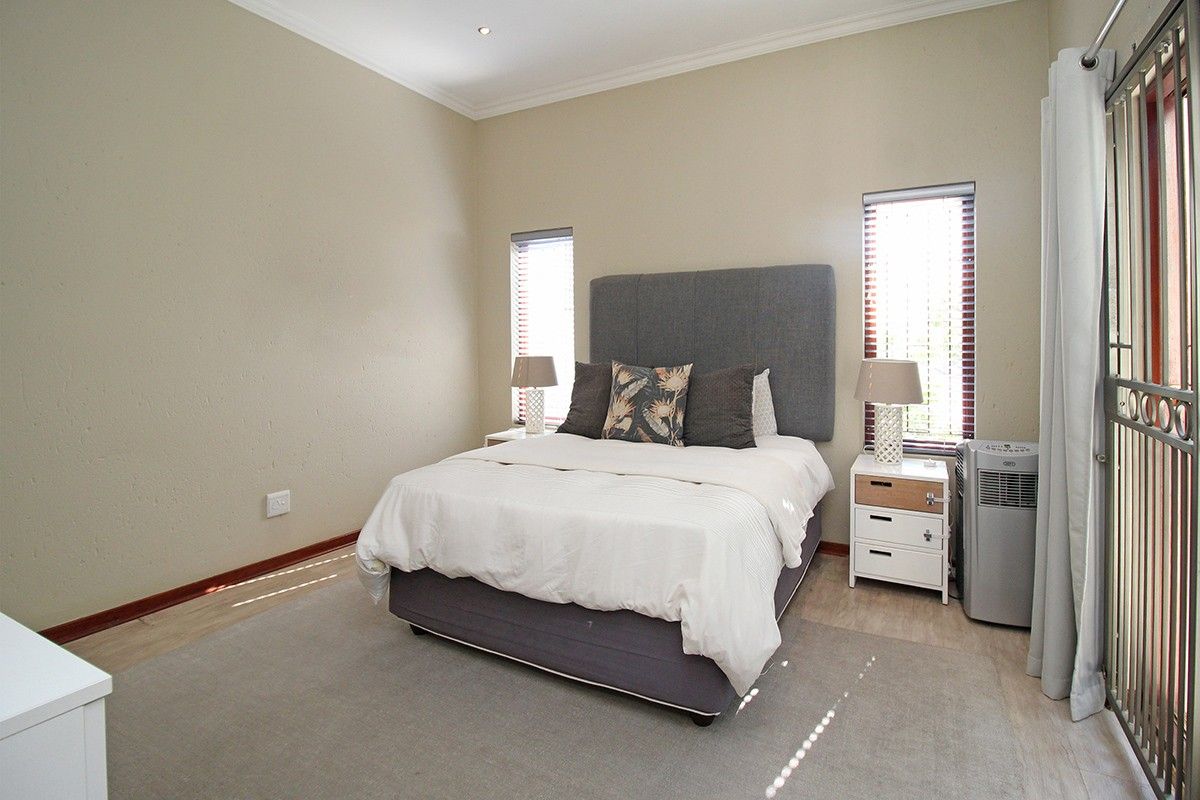 A well-maintained bedroom featuring neutral walls, light flooring, recessed downlighting, and dual windows fitted with venetian blinds and a security gate.