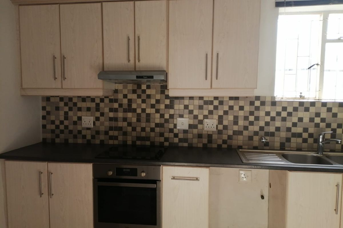 Functional kitchen featuring light wood-finish cabinetry, a mosaic tile backsplash, built-in oven, electric hob, and a stainless steel sink with a window view.