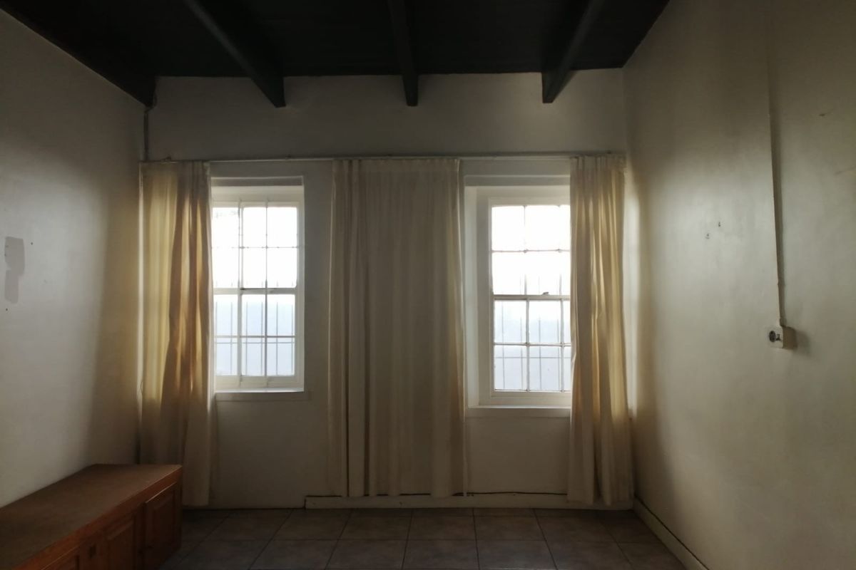 An empty living room featuring exposed timber ceiling beams, tiled flooring, and dual sash windows with security bars.