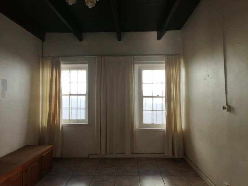 An empty living room featuring exposed timber ceiling beams, tiled flooring, and dual sash windows with security bars.
