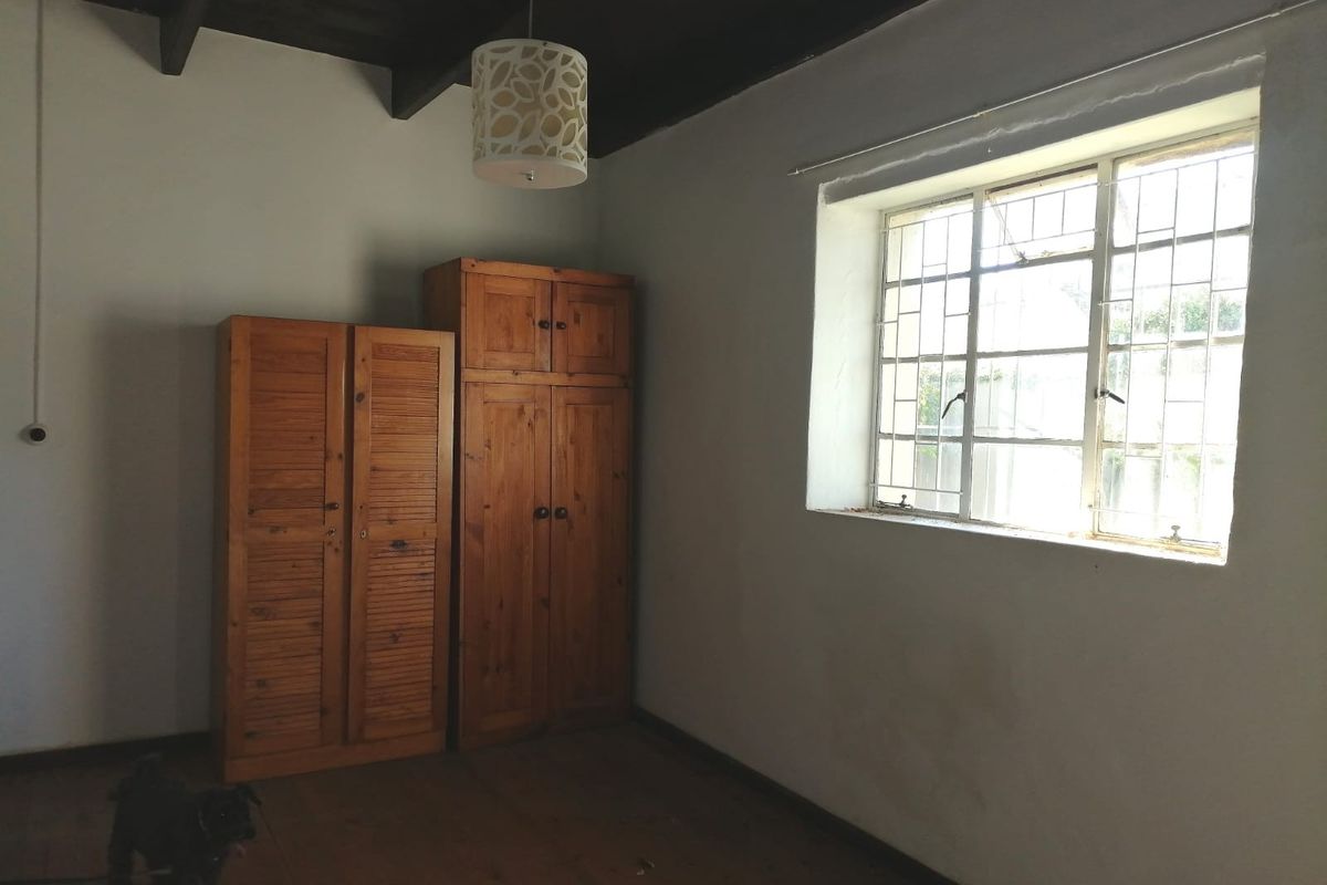 A bedroom featuring exposed timber ceiling beams, timber flooring, and a steel-framed window with security bars.