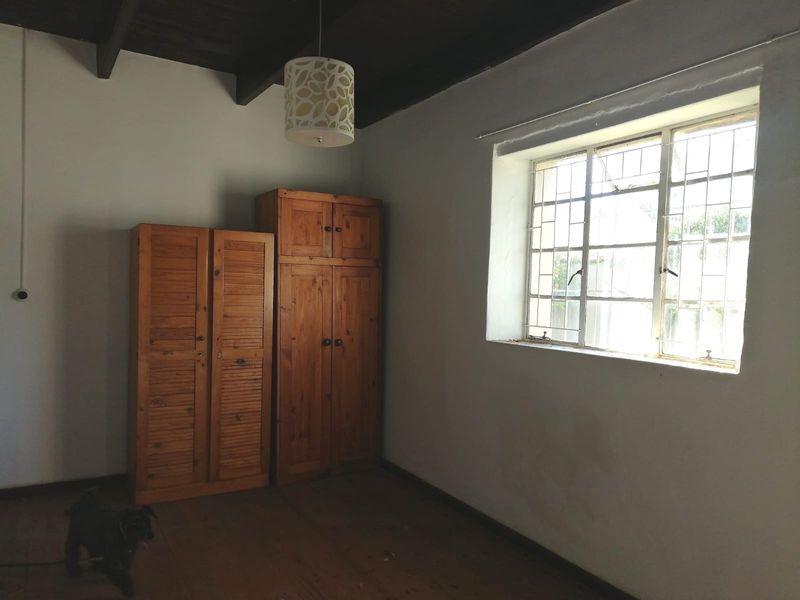 A bedroom featuring exposed timber ceiling beams, timber flooring, and a steel-framed window with security bars.