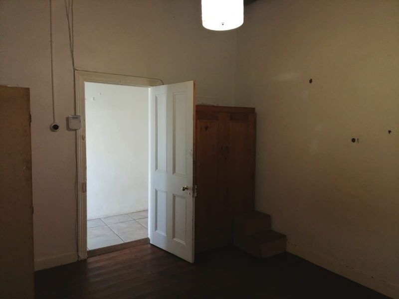 A vacant bedroom featuring original timber flooring and a classic panelled door, requiring cosmetic updates to the wall surfaces.