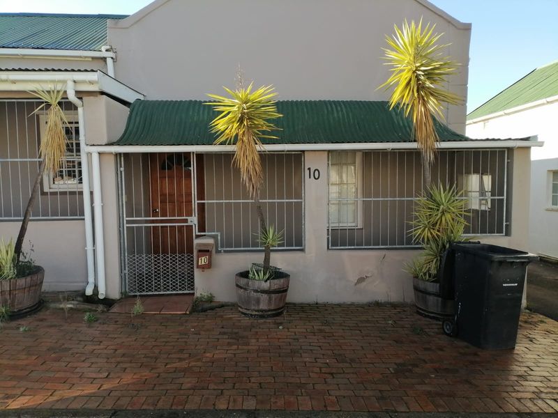 Front elevation of a residential property featuring a brick paved entrance, corrugated metal roof covering, and security bars on windows and doors.