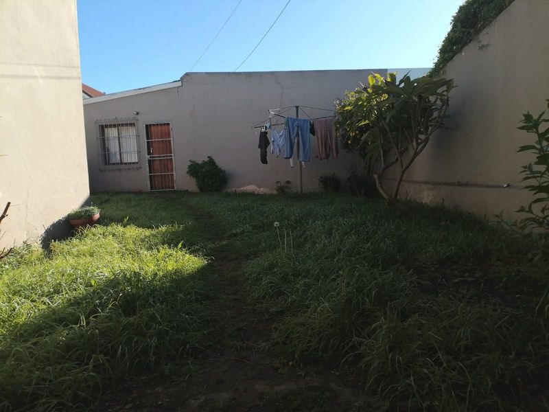 A rear garden area featuring a lawn, boundary walls, and access to the property via a security gate.