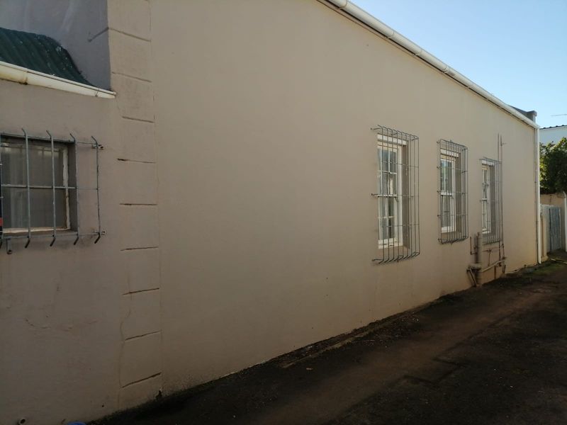 Side elevation of the property featuring painted masonry walls, security bars on sash windows, and functional guttering systems.
