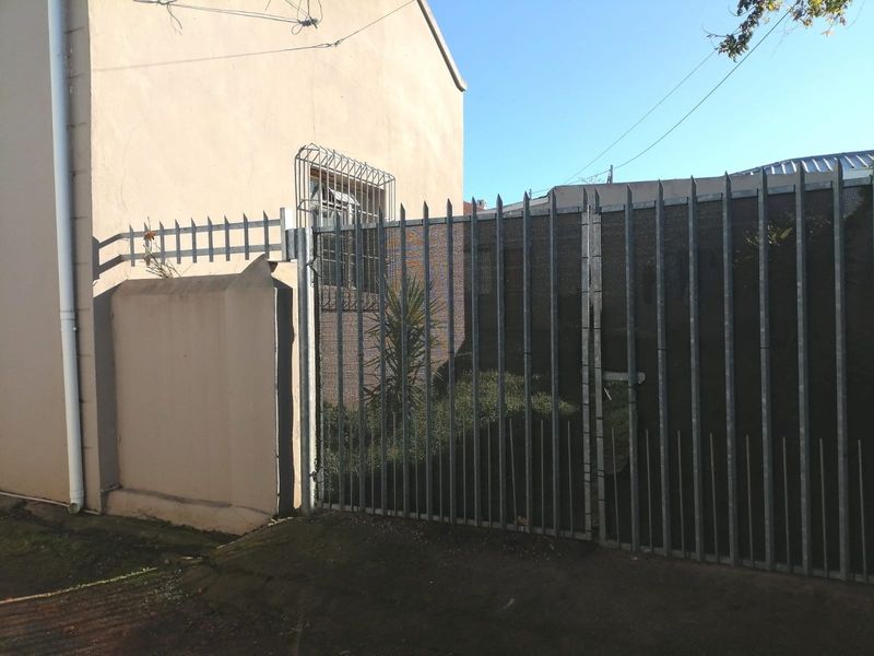 Front exterior view of the property featuring a metal security gate, perimeter wall, and security bars on the window.