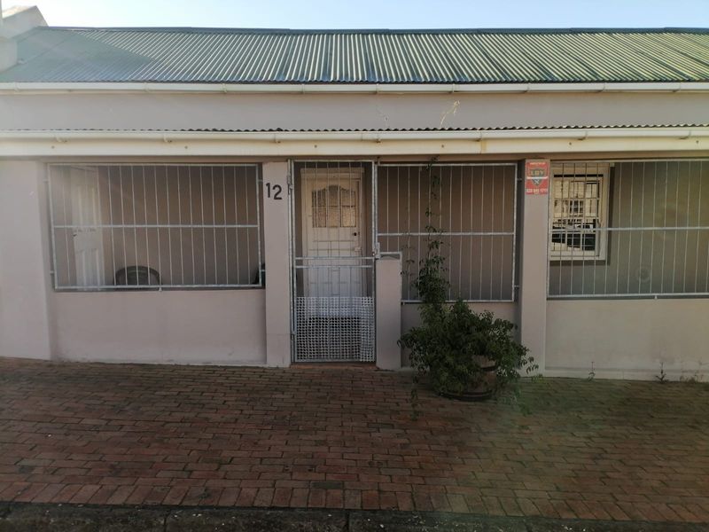 Front facade of a residential property featuring a corrugated metal roof, brick paving, and security bars on windows and entrance.