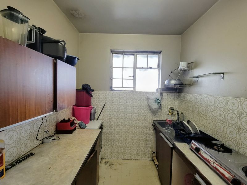 A compact, dated kitchen featuring original cabinetry, tiled backsplash, and a gas hob, offering significant potential for modernization and renovation.