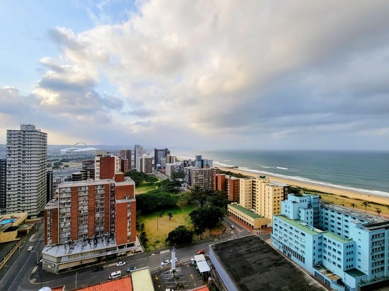 Elevated panoramic view overlooking the coastal city skyline, urban buildings, and the adjacent beach shoreline.