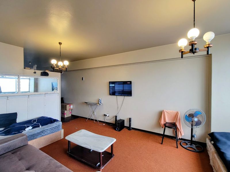 Spacious living area featuring carpet flooring, wall-mounted television, and dual ceiling light fixtures, offering a blank canvas for potential interior updates.