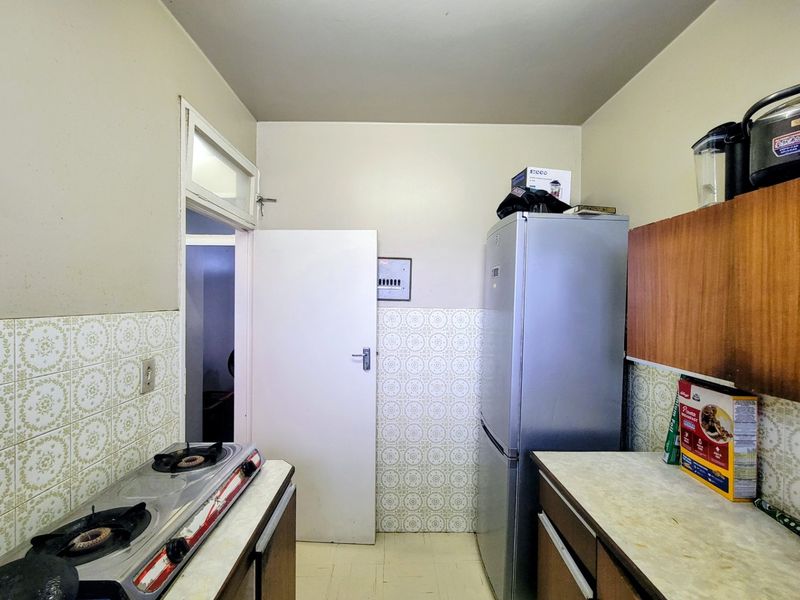 A compact kitchen featuring dated ceramic wall tiles, laminate countertops, and a built-in gas hob, offering potential for modernization.