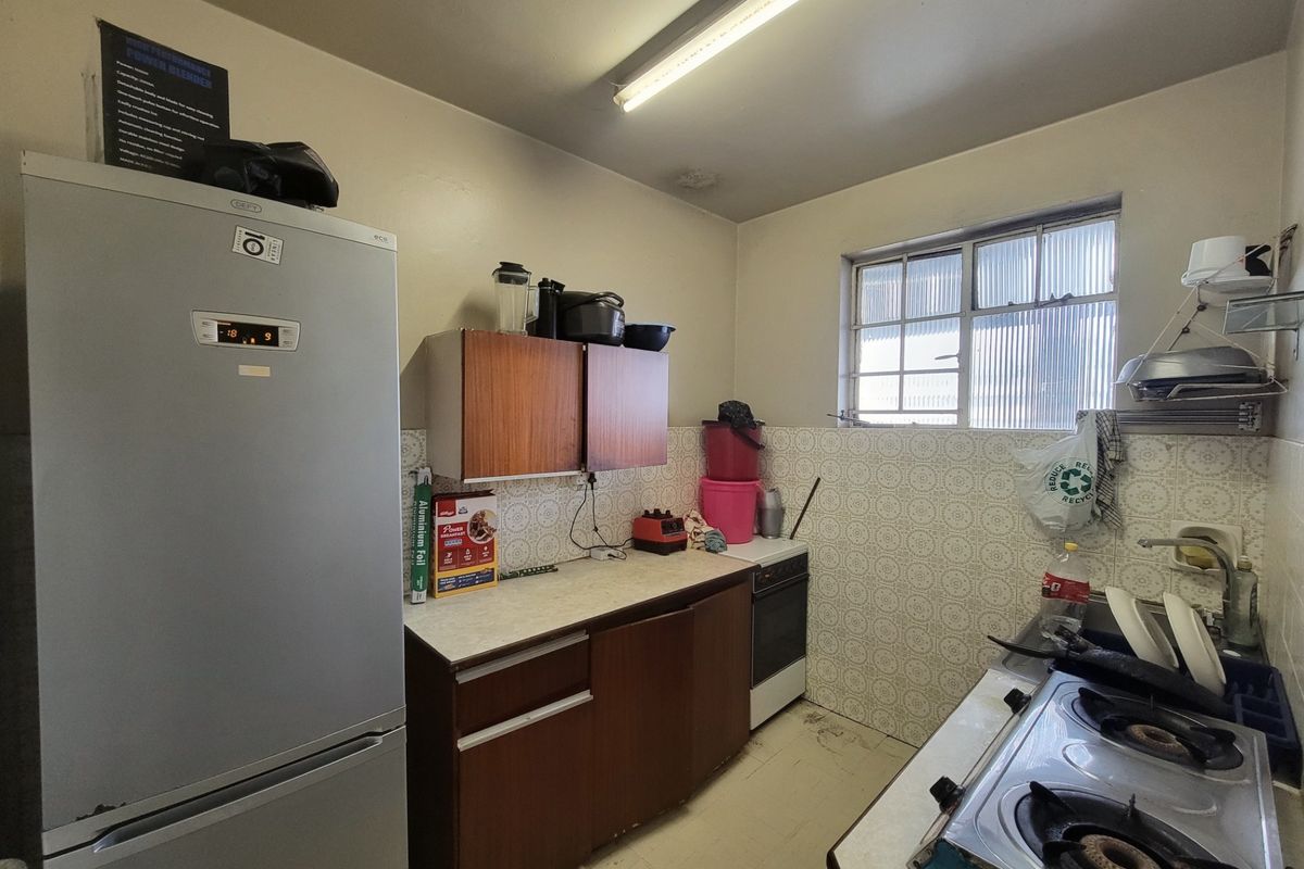 A dated kitchen featuring original cabinetry, laminate countertops, a freestanding stove, and a tiled backsplash, offering significant potential for modernization and renovation.