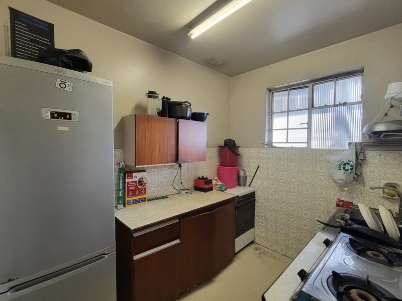 A dated kitchen featuring original cabinetry, laminate countertops, a freestanding stove, and a tiled backsplash, offering significant potential for modernization and renovation.