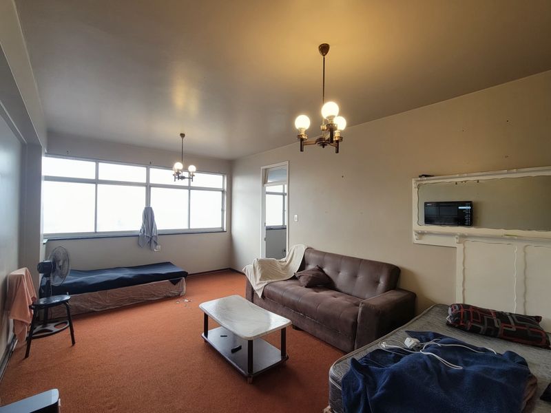Spacious living area featuring large windows, carpet flooring, and classic ceiling light fixtures, offering a blank canvas for potential renovation and modernization.