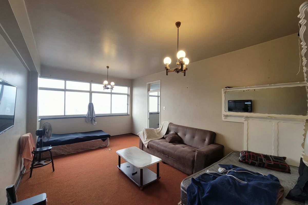 Spacious living area featuring large windows, carpet flooring, and classic ceiling light fixtures, offering a blank canvas for potential renovation and modernization.