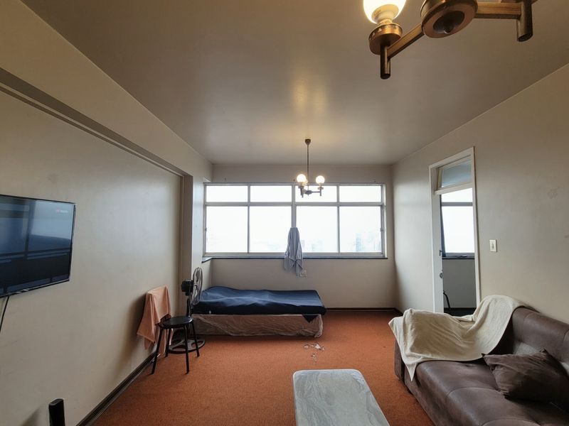 A bedroom featuring large windows, carpeted flooring, and a central ceiling light fixture, offering a functional space with potential for cosmetic updates.