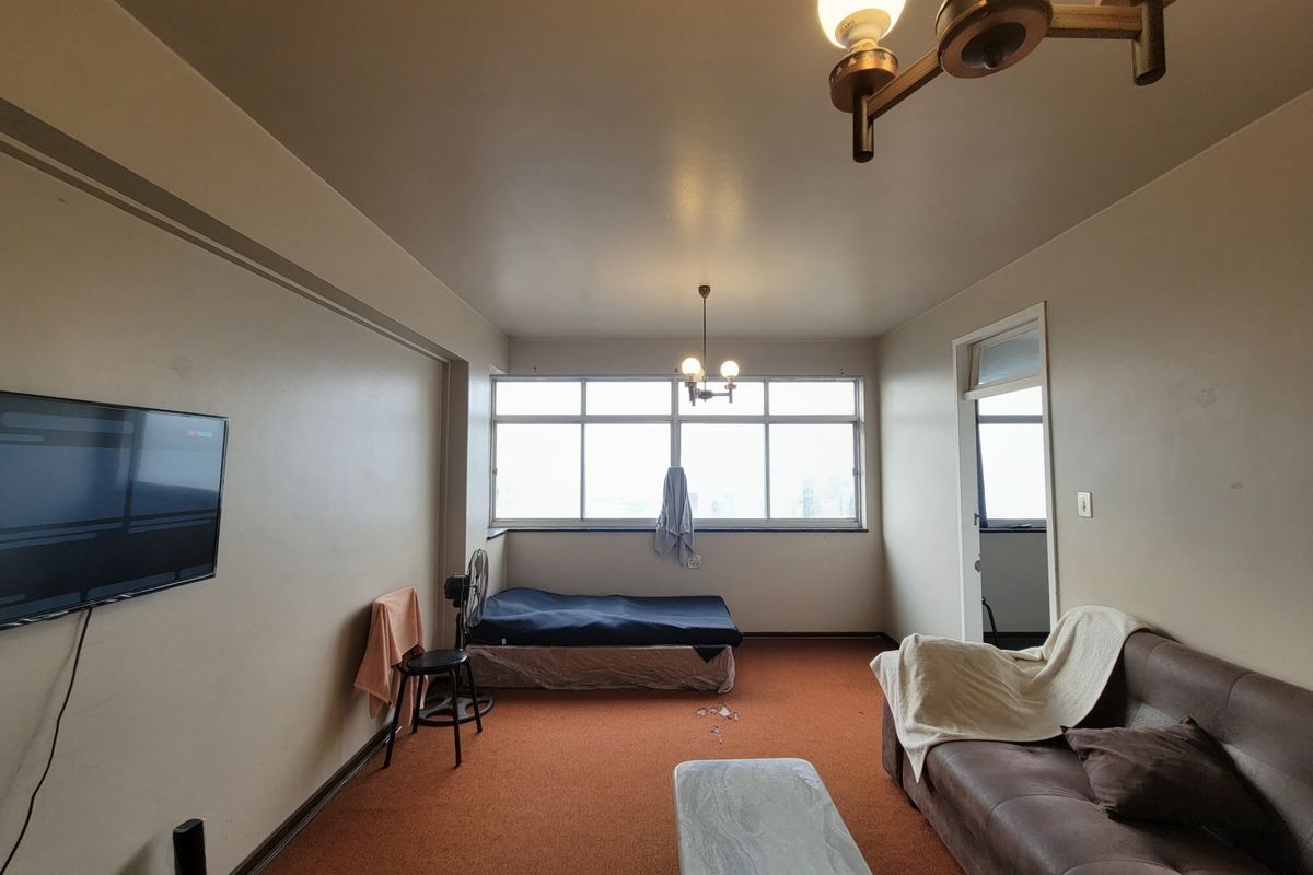 A bedroom featuring large windows, carpeted flooring, and a central ceiling light fixture, offering a functional space with potential for cosmetic updates.