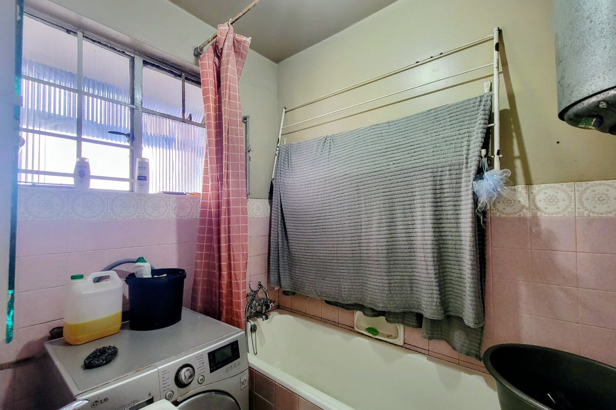 A functional bathroom featuring a bathtub, tiled walls, and a wall-mounted drying rack, requiring cosmetic updates to improve its overall condition.