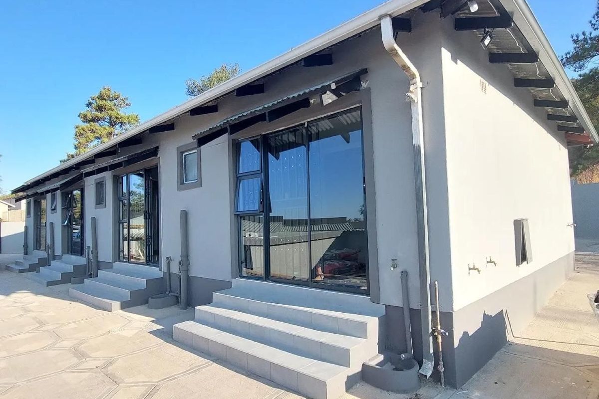 Rear exterior view of the property featuring modern grey facade, tiled steps, and aluminium sliding doors leading to a paved patio area.