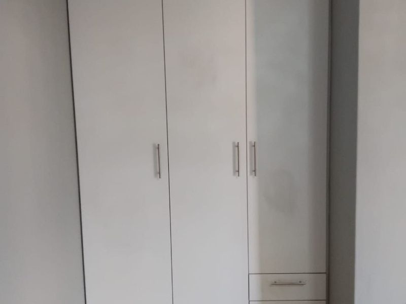 A clean bedroom space featuring a modern white built-in wardrobe with integrated drawers and neutral tiled flooring.