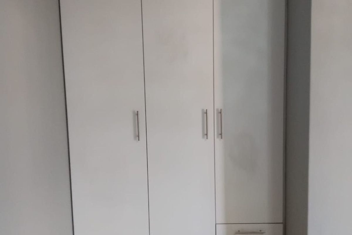 A clean bedroom space featuring a modern white built-in wardrobe with integrated drawers and neutral tiled flooring.