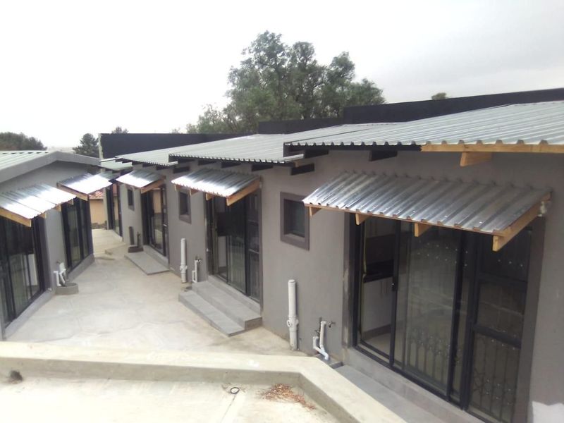 Rear view of a modern residential building featuring multiple sliding glass door entrances, corrugated metal awnings, and a concrete patio area.