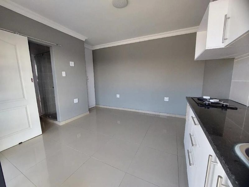An open-plan living area featuring tiled floors, a modern kitchen with granite countertops and a built-in hob, leading to an adjacent bathroom.
