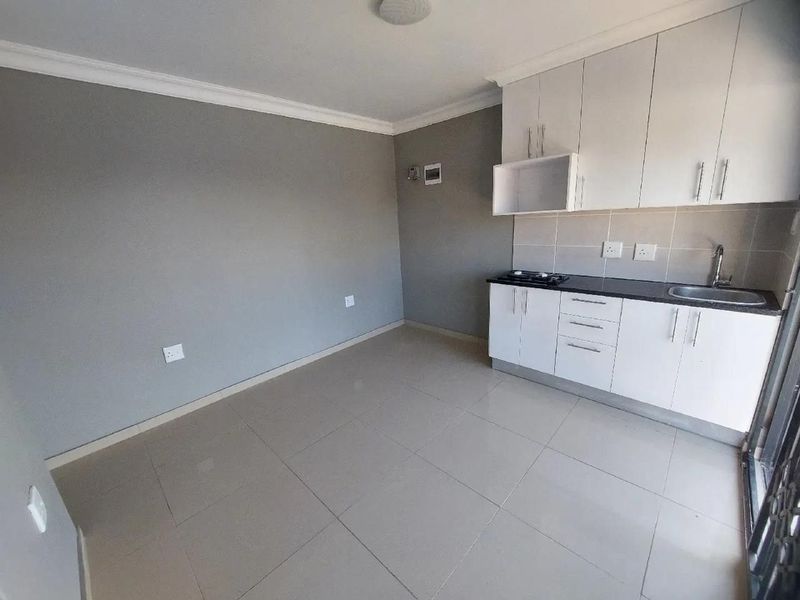 A compact, modern kitchen featuring white cabinetry, dark stone countertops, a built-in hob, and neutral tiled flooring in an open-plan living space.