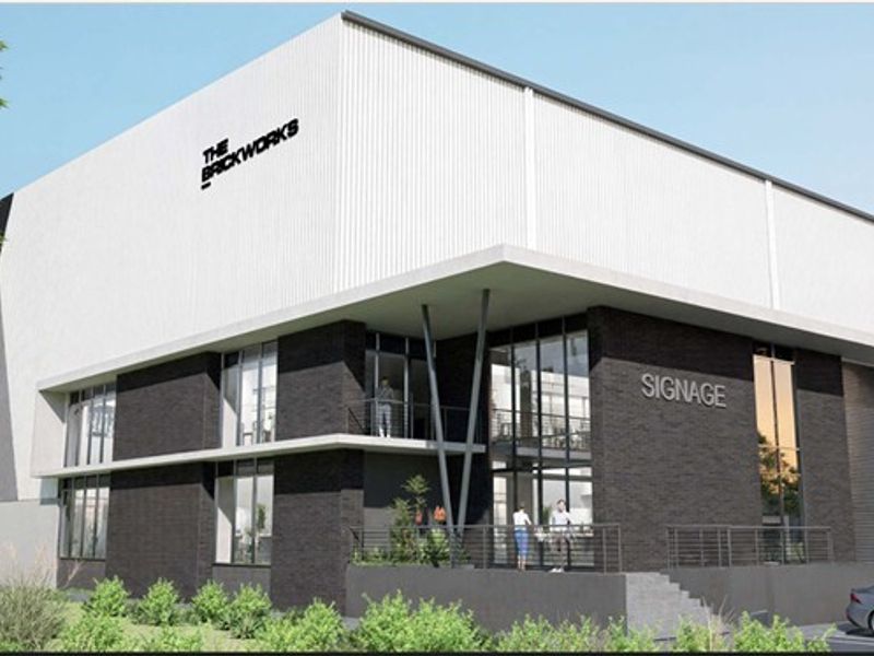 Modern industrial building facade featuring a combination of dark brickwork, white metal cladding, and expansive glass windows with a prominent entrance balcony.