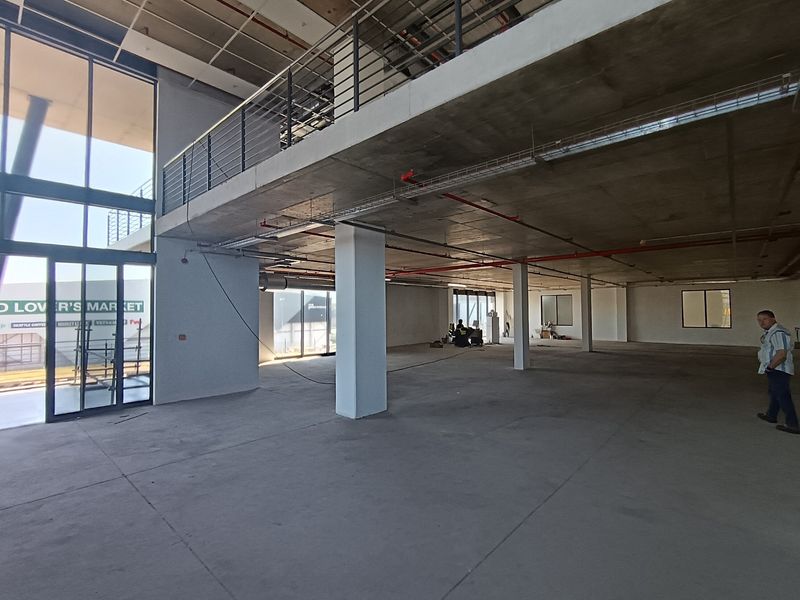 Spacious open-plan industrial unit featuring a mezzanine level, exposed concrete ceilings, and large glass windows, offering a versatile blank canvas for commercial use.