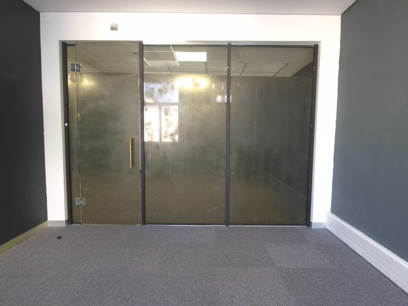 An empty office space featuring dark grey walls, carpet flooring, and a modern glass partition wall with a glass door.
