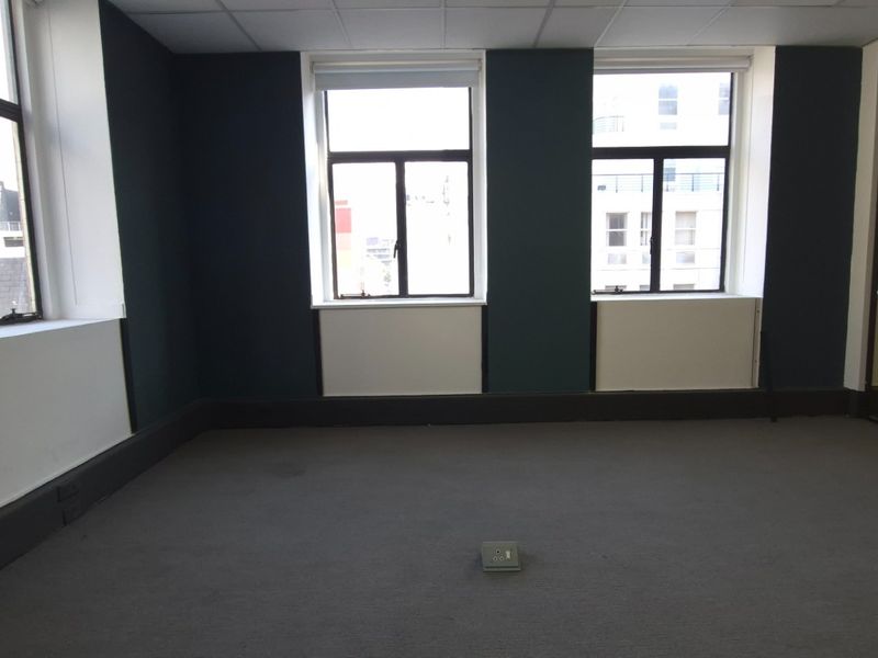 An empty commercial office space featuring carpeted flooring, a suspended ceiling, and a glass partition wall with natural light from multiple windows.