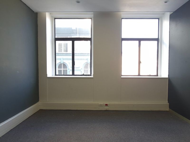 An empty office space featuring dark grey accent walls, neutral carpeting, and dual windows providing natural light.