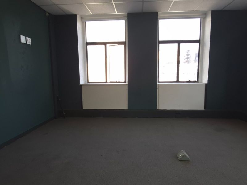 A vacant commercial office space featuring dark painted walls, carpeted flooring, and large windows providing natural light.