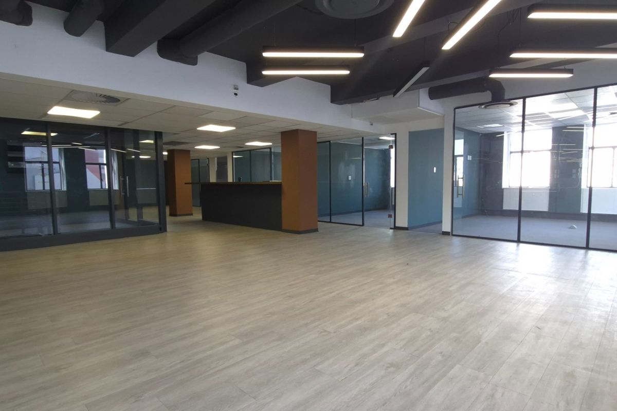 Modern open-plan commercial office space featuring glass-partitioned meeting rooms, laminate flooring, and contemporary exposed ceiling with integrated linear lighting.