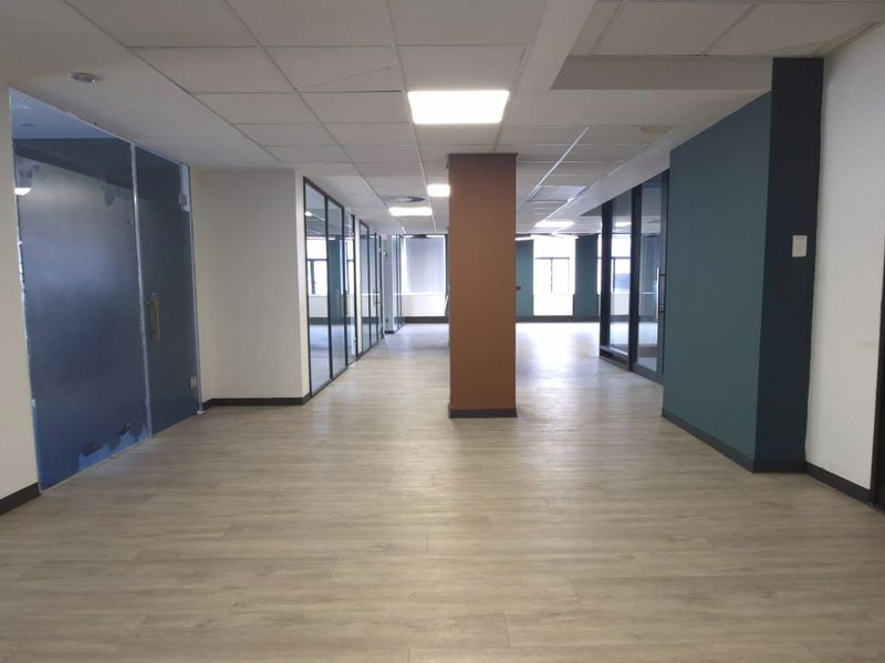 A spacious, modern open-plan office area featuring glass partitions, wood-look laminate flooring, and a clean, professional suspended ceiling design.