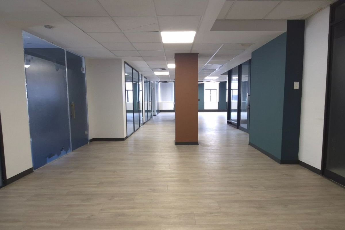 A spacious, modern open-plan office area featuring glass partitions, wood-look laminate flooring, and a clean, professional suspended ceiling design.