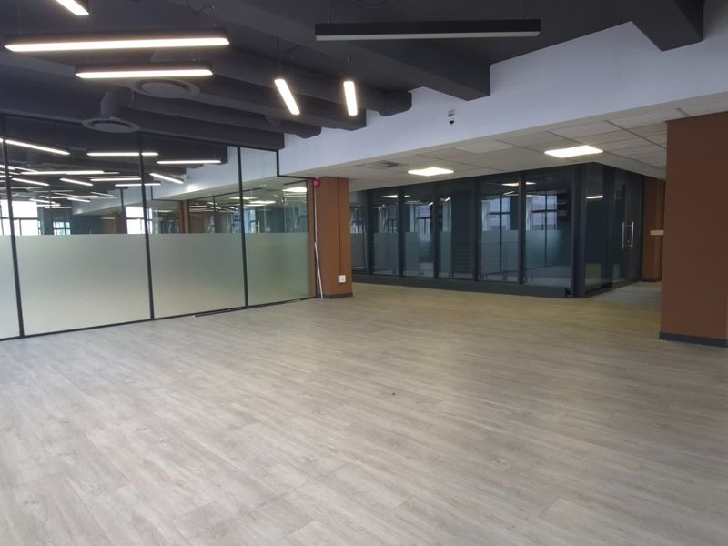 Modern open-plan commercial office space featuring glass partitioning, contemporary lighting, and high-quality laminate flooring in a professional, well-maintained environment.