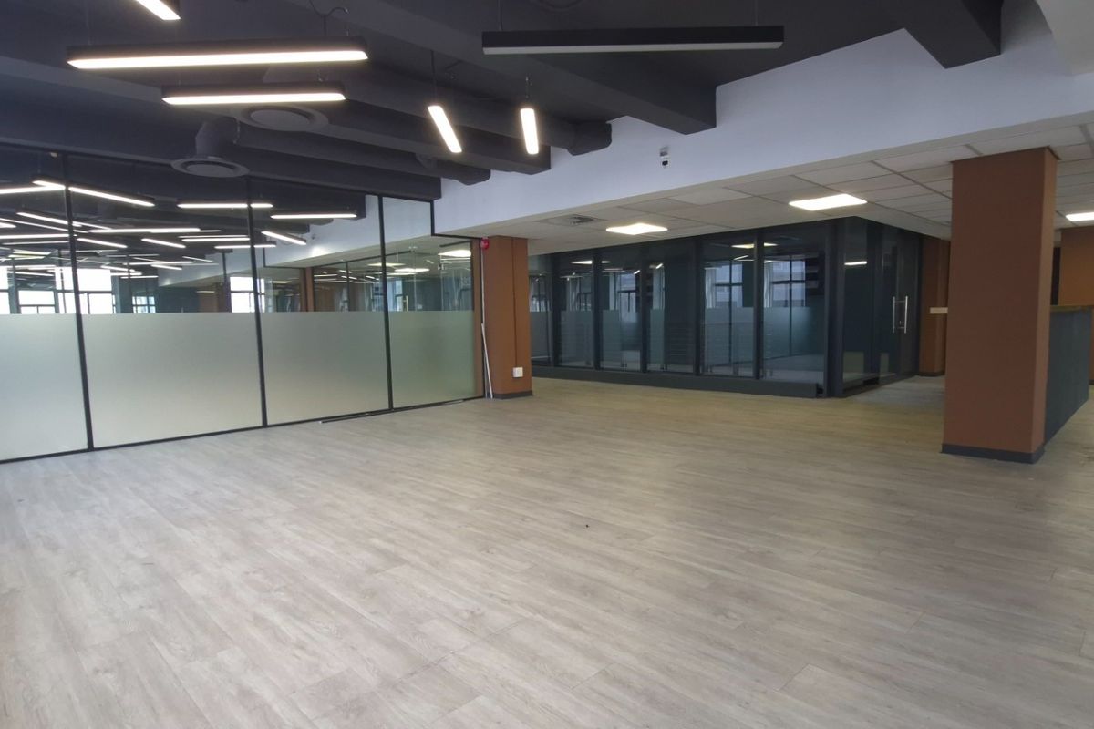 Modern open-plan commercial office space featuring glass partitioning, contemporary lighting, and high-quality laminate flooring in a professional, well-maintained environment.