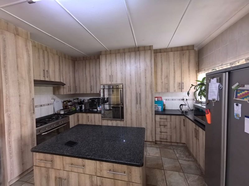 A functional kitchen featuring wood-look cabinetry, granite countertops, a central island, and built-in appliances including an oven and gas hob.