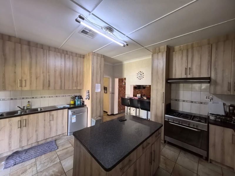 A functional kitchen featuring wood-look cabinetry, a central island with a stone countertop, gas stove, and tiled flooring, offering ample storage and workspace.