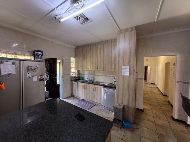 A functional kitchen featuring wood-look cabinetry, granite countertops, double sink, and tiled finishes throughout, providing a practical workspace with direct access to the hallway.