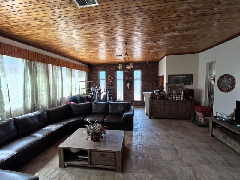 Spacious living room featuring a distinctive timber ceiling, exposed brick wall, and tiled flooring, offering a rustic aesthetic with potential for modern updates.