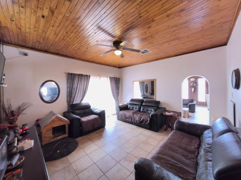 Spacious living room featuring a warm timber tongue and groove ceiling, ceramic tiled flooring, and an arched entryway leading to adjacent living space.