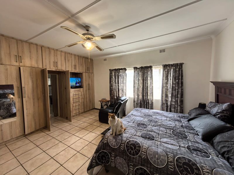 Spacious bedroom featuring extensive built-in wooden cabinetry, tiled flooring, and a ceiling fan, offering ample storage and functional living space.